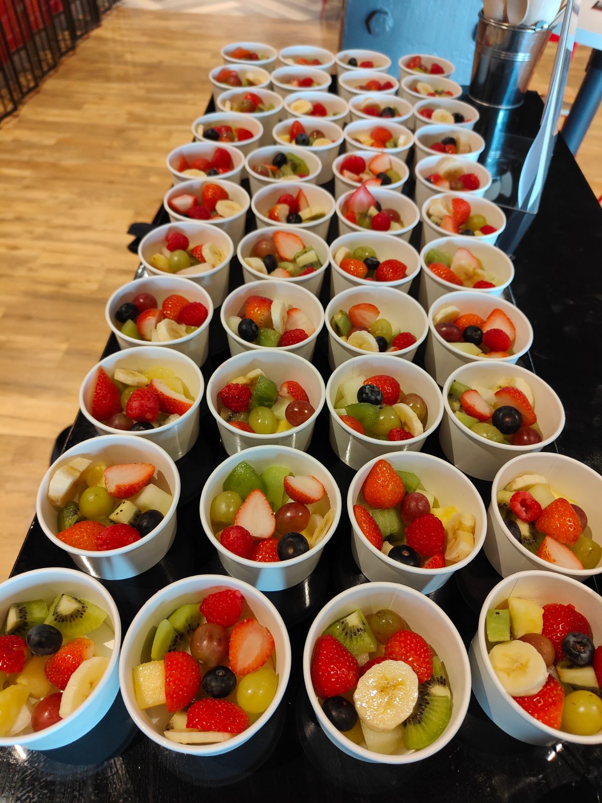 Rows of freshly prepared fruit bowls laid out on a breakfast bar at a corporate event