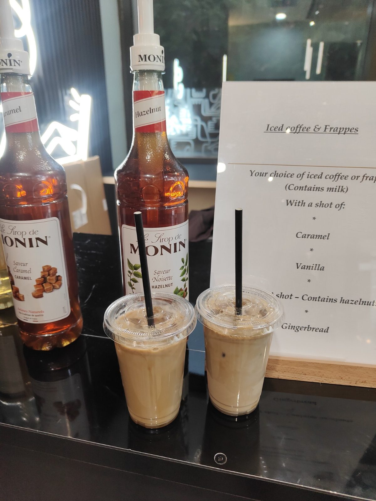 Two iced coffees beside caramel and hazelnut Monin syrups and the iced coffee menu