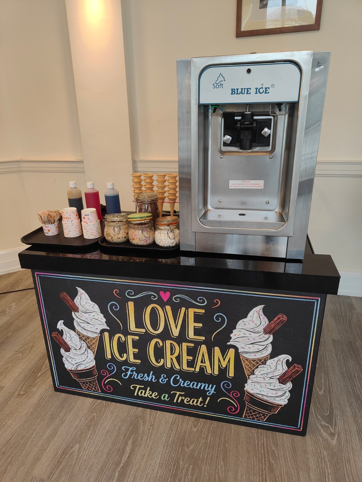 Ice cream bar with a soft serve machine, cones, sauces and jars of toppings