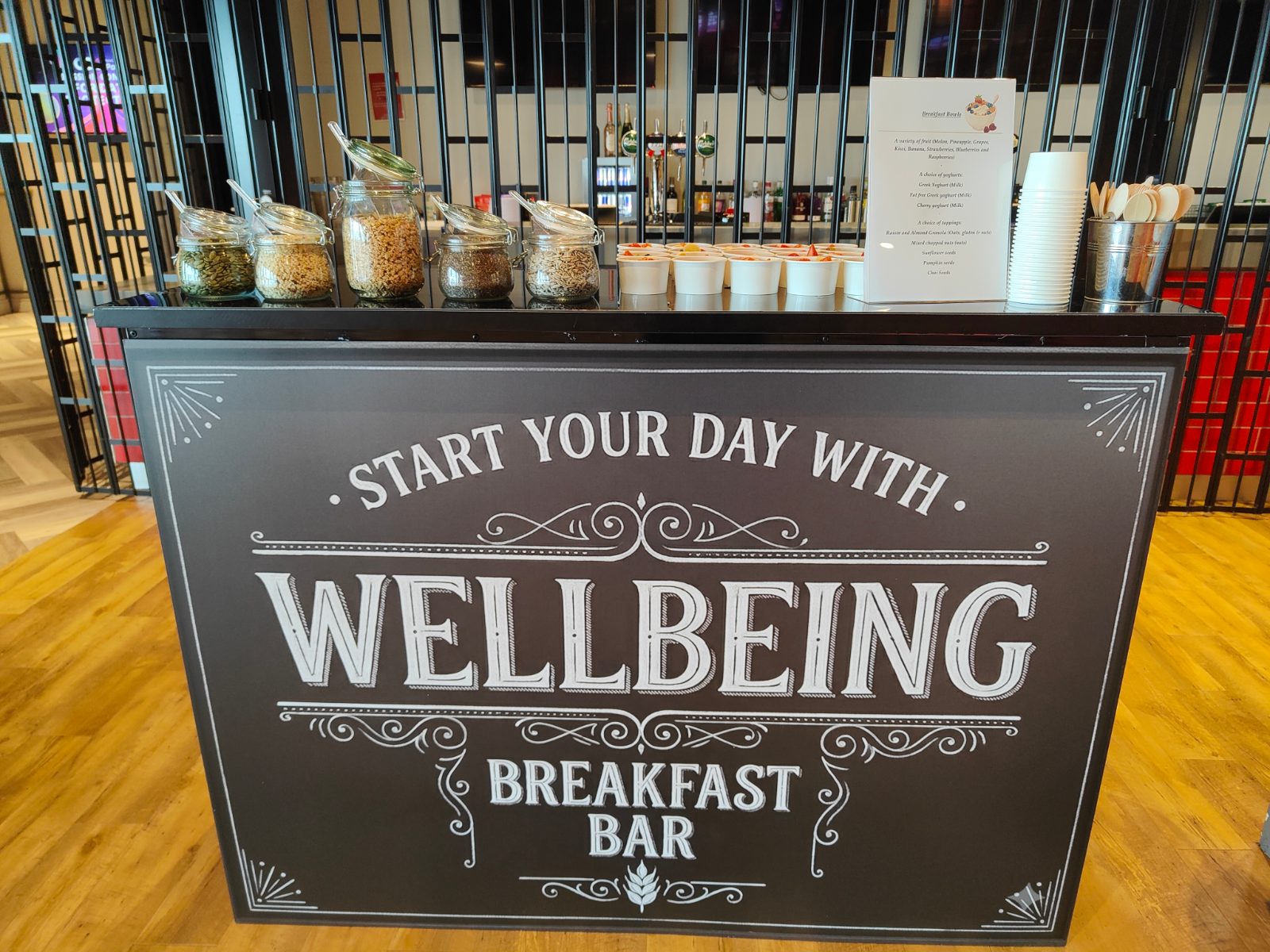 Wellbeing breakfast bar with jars of granola, nuts and seeds, fruit bowls and a menu card